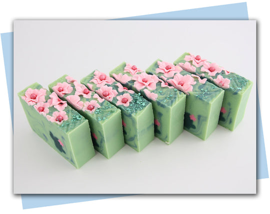 Bars of soap with pink flowers on soap and a green cactus embeds in a green swirl