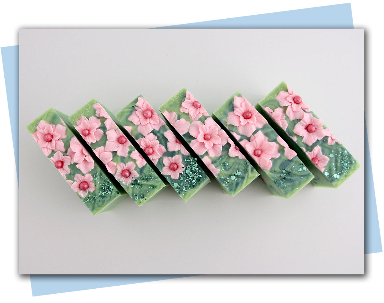 Bars of soap with pink flowers on soap and a green cactus embeds in a green swirl