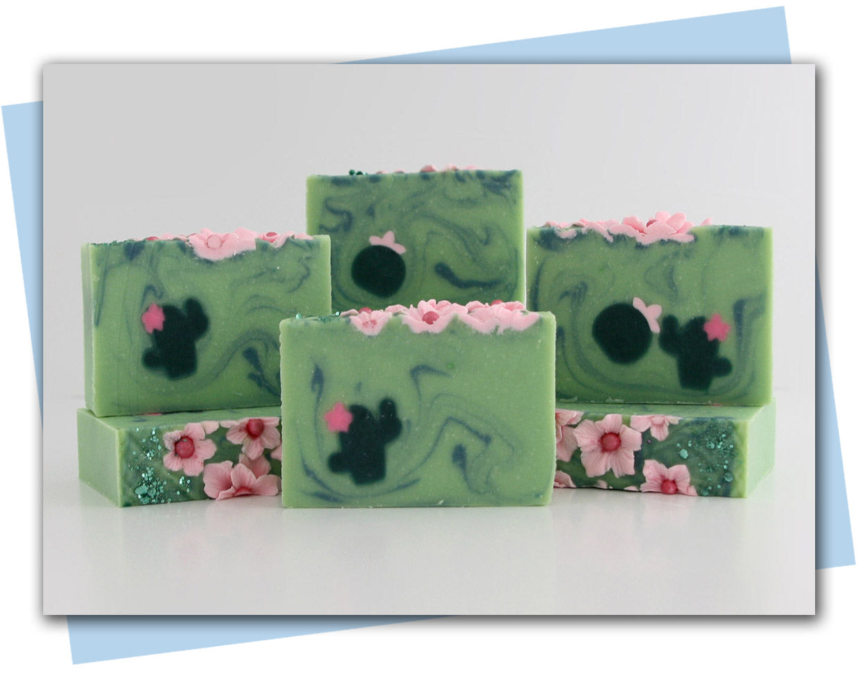 Bars of soap with pink flowers on soap and a green cactus embeds in a green swirl