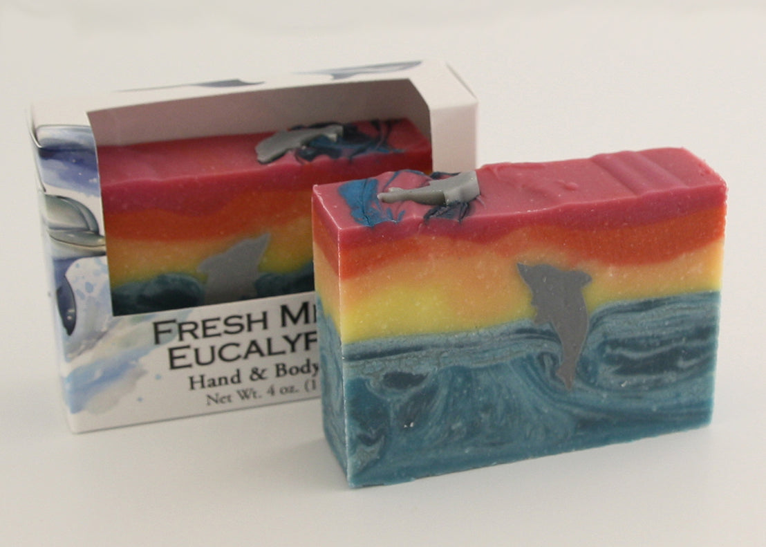 Bars of soap in custom packaging with with a dolphin jumping out of the water in  a sunset design
