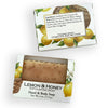 Two boxed bars of exfoliating hand and body soap on a white background. The packaging features lemon and wicker basket illustrations, with one box showing the soap bar through a clear window.