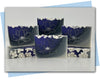 Purple to gray to white ombre bars of soap with white flowers decorating the top and a magnolia flower stamp on the face of the bar
