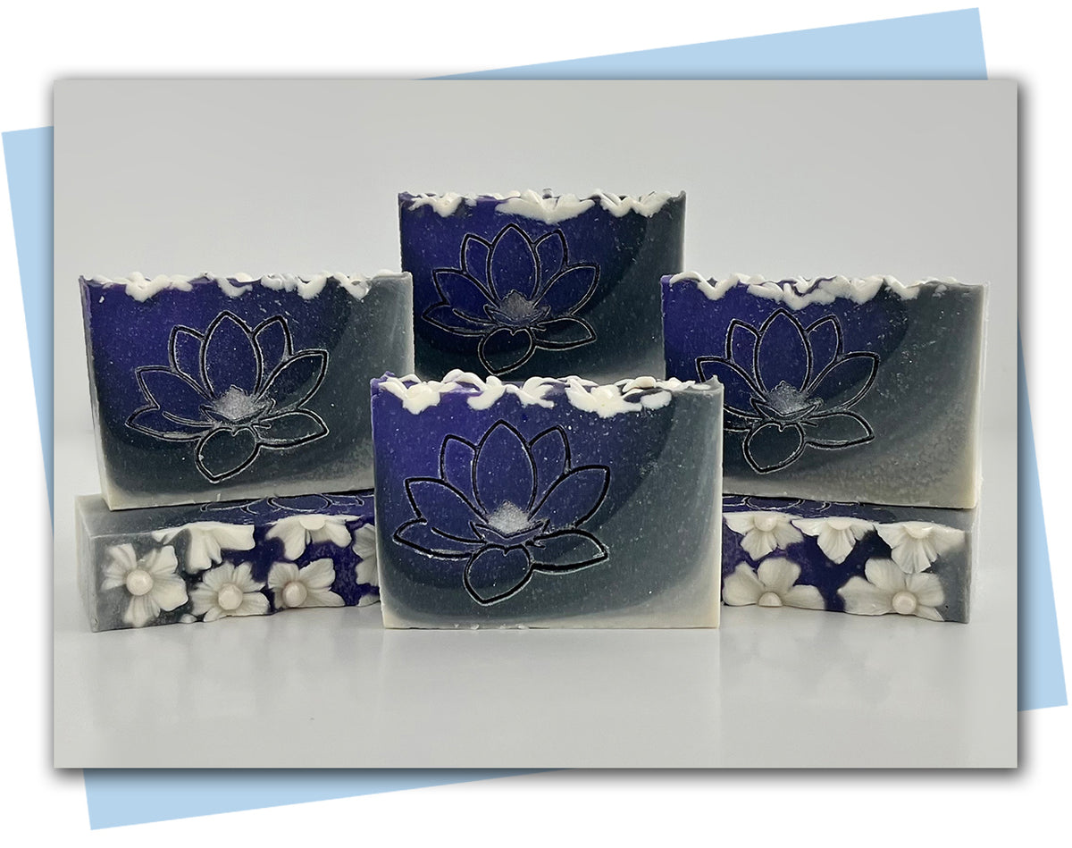 Purple to gray to white ombre bars of soap with white flowers decorating the top and a magnolia flower stamp on the face of the bar