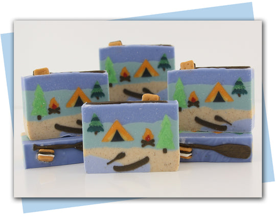 bars of soap with a camping themed design: tent, camp fire, canoe on lake and trees in forest.