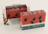 Bars of soap in custom packaging made to look like a watermelon with green bottom layer and black seeds in the pink layer